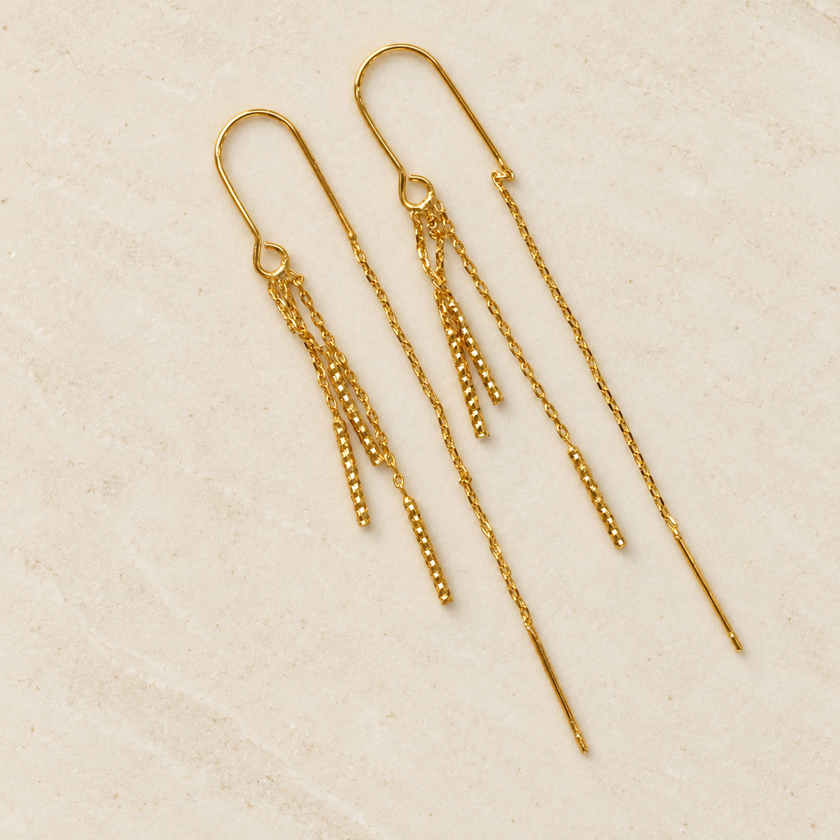 Gold-tone pair of dangle chain earrings on a light stone surface