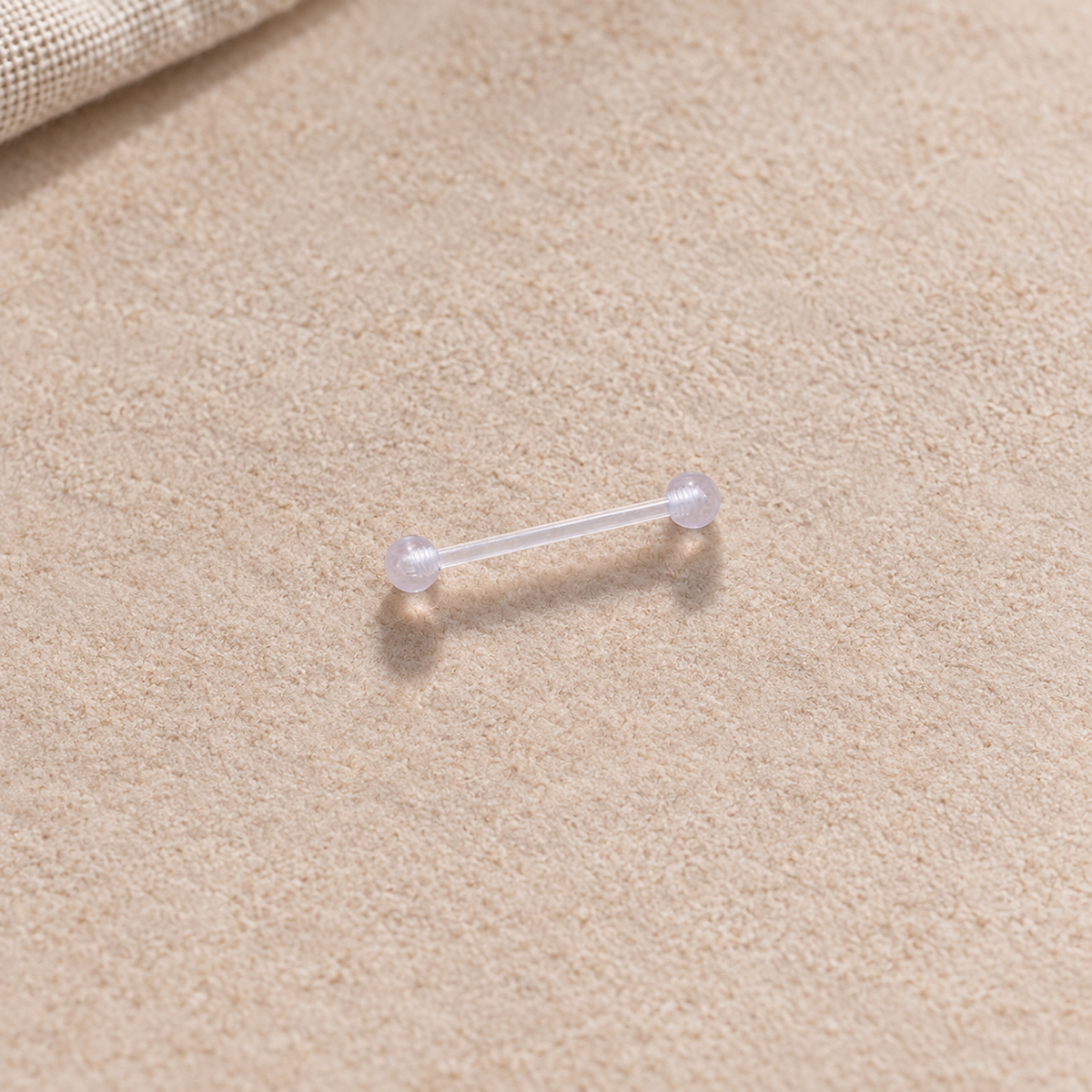 Clear nipple retainer barbell on a neutral textured surface