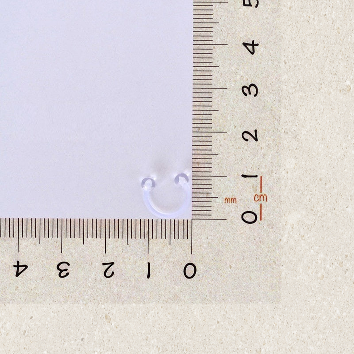 Clear horseshoe piercing retainer beside a ruler for size reference