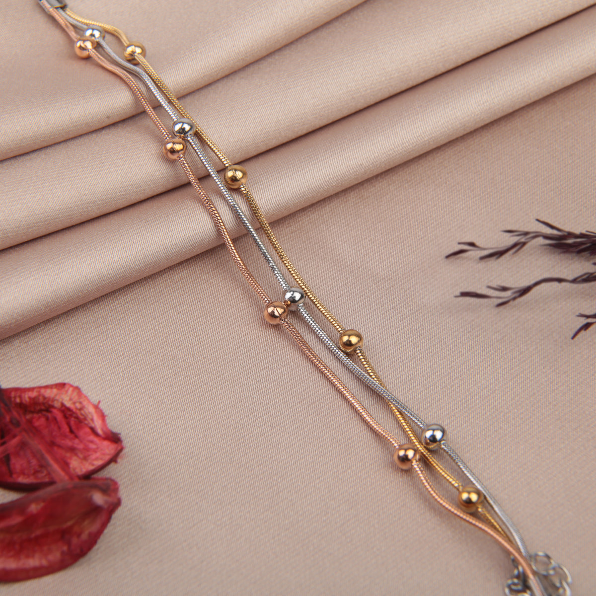 Set of three beaded bracelets in gold, silver and rose gold tones on a fabric background