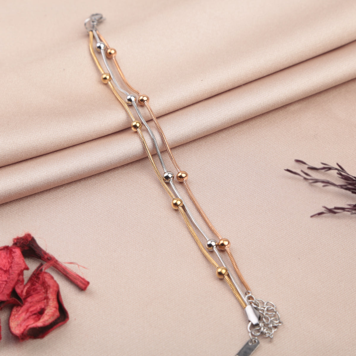 Set of three beaded bracelets in gold, silver and rose gold tones on a fabric background
