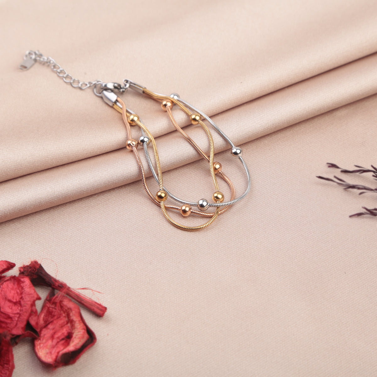 Set of three beaded bracelets in gold, silver and rose gold tones on a fabric background