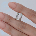 Two silver-tone hoops with round pastel-coloured stones in bezel-style settings held across two fingers.