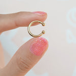Gold mini flat ear cuff held between fingers, showing both rounded ends