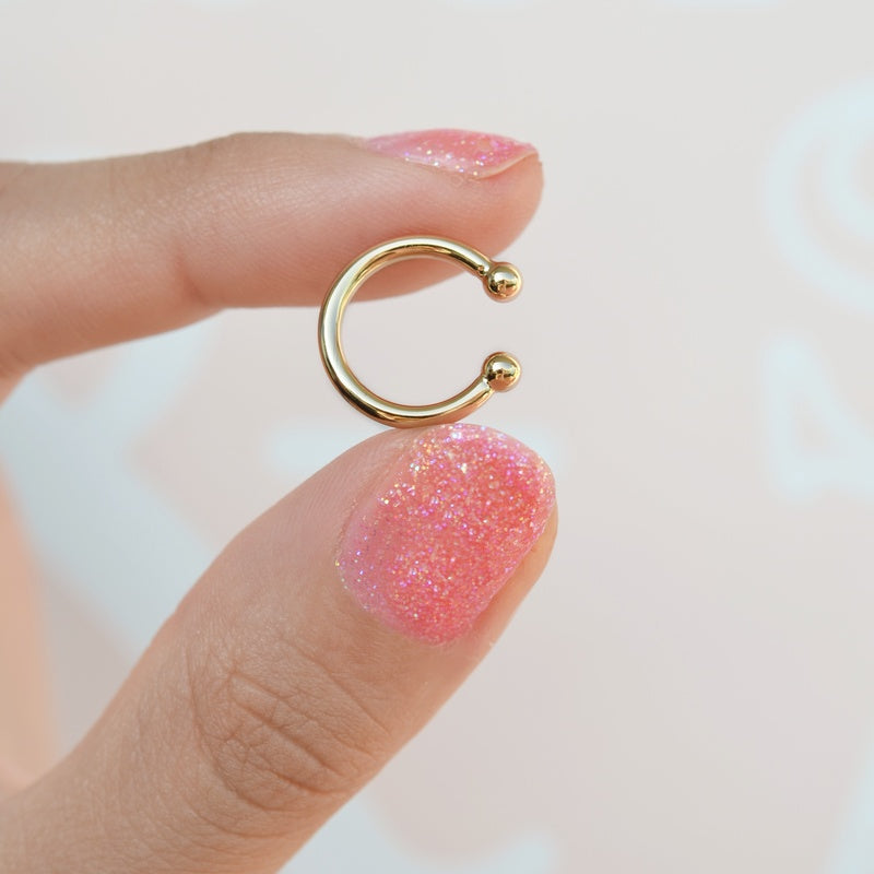 Gold mini flat ear cuff held between fingers, showing both rounded ends