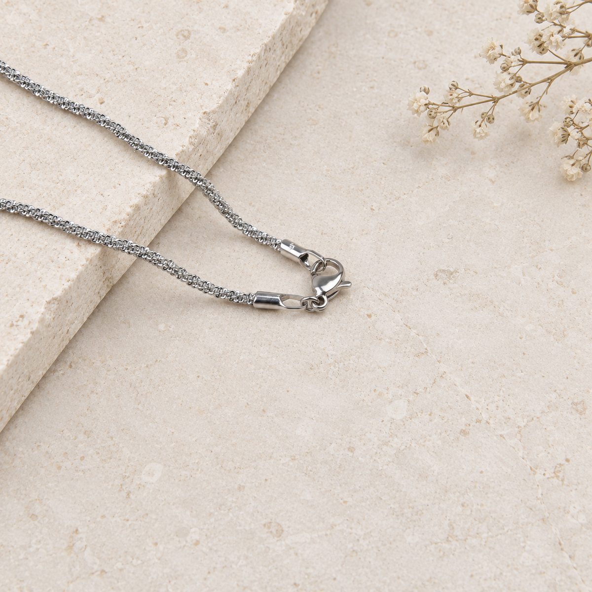 Silver glitter chain necklace arranged beside dried flowers