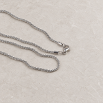 Silver glitter chain necklace arranged on a light stone surface