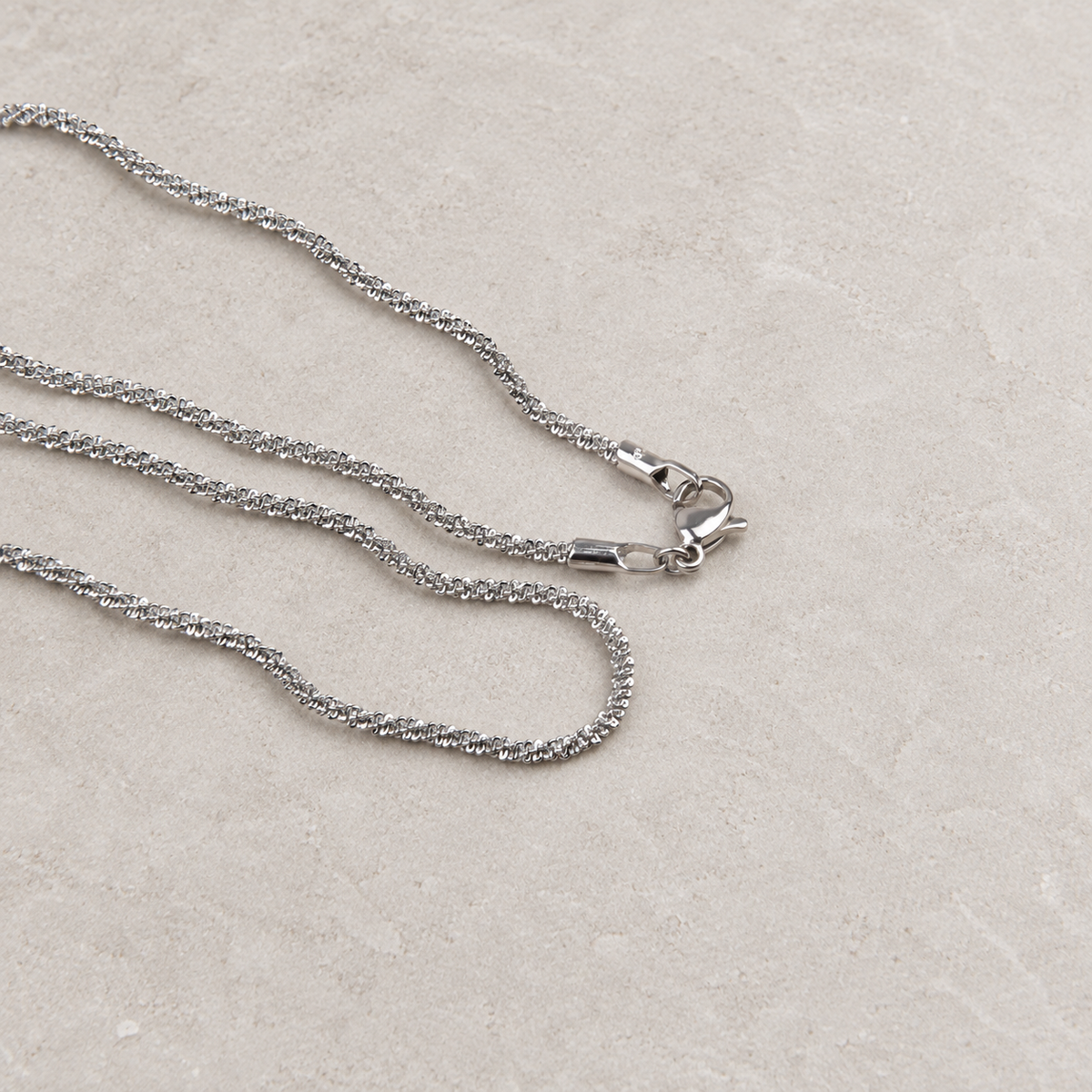 Silver glitter chain necklace arranged on a light stone surface