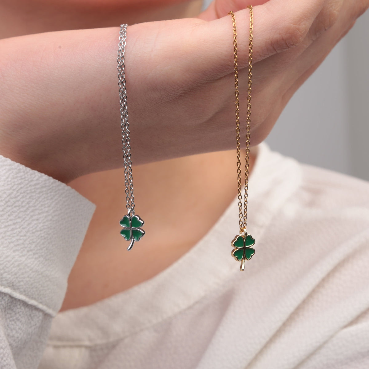 Gold and silver clover pendant necklaces held side by side