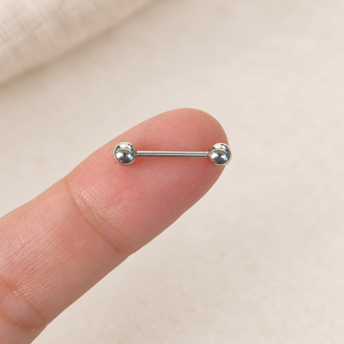 Straight Nipple Barbell with Ball Ends, 16G, 18mm, Single - silver-tone barbell held on a fingertip