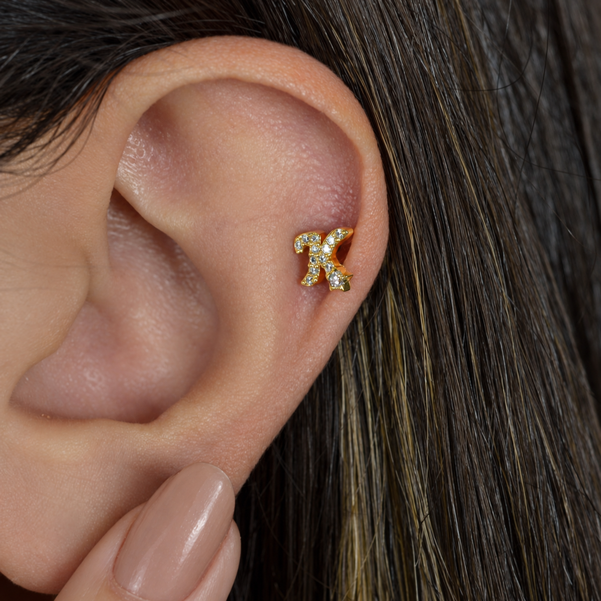 Gold zircon letter K piercing stud shown on the ear