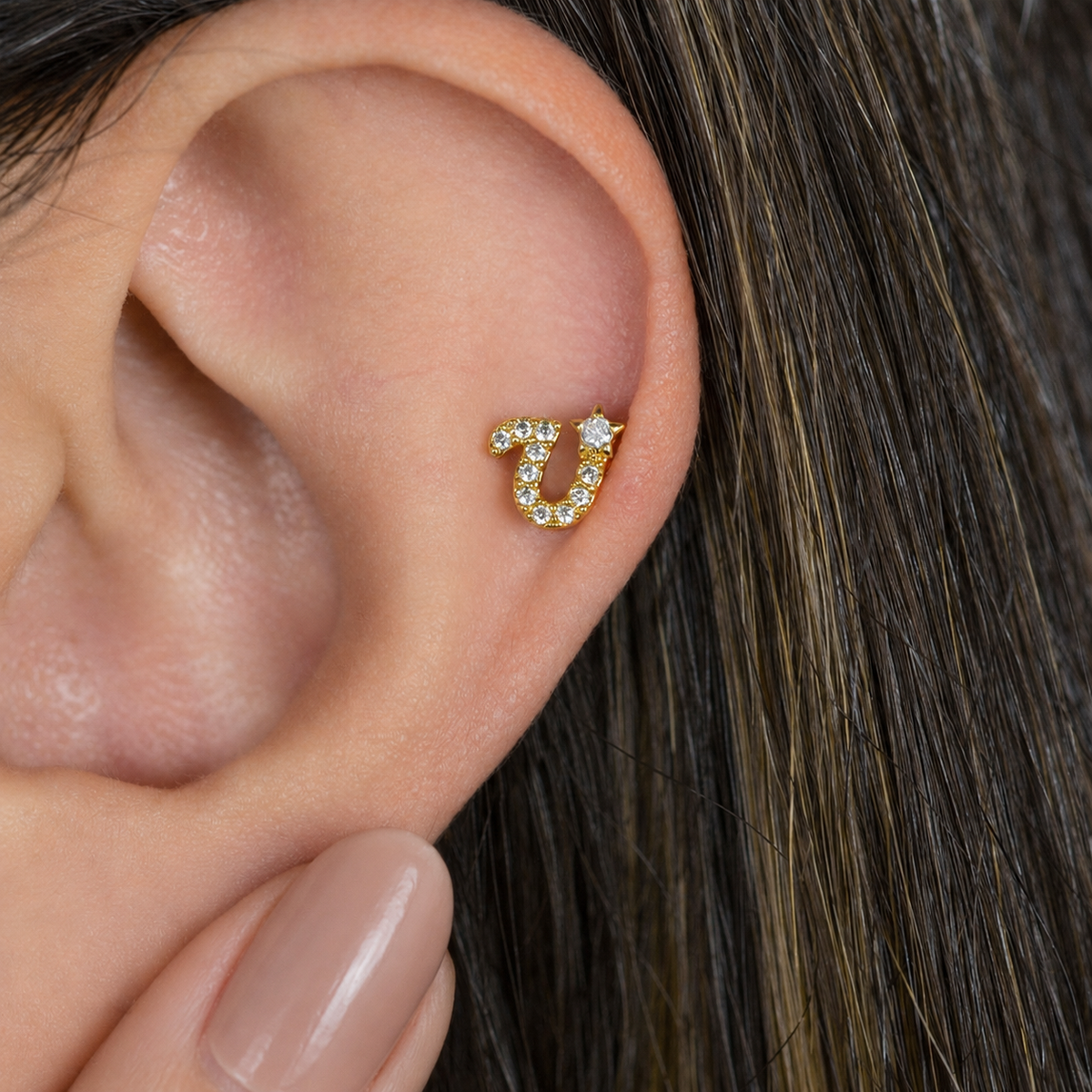 Gold zircon letter U piercing stud shown on the ear