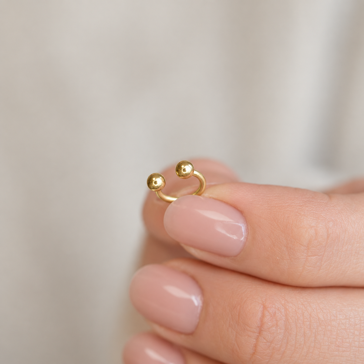 Gold horseshoe barbell held between fingers