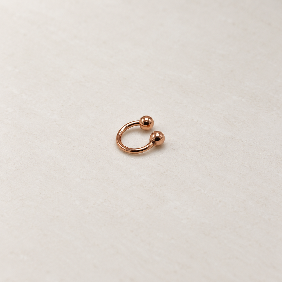 Rose gold ball-end horseshoe barbell on a neutral background