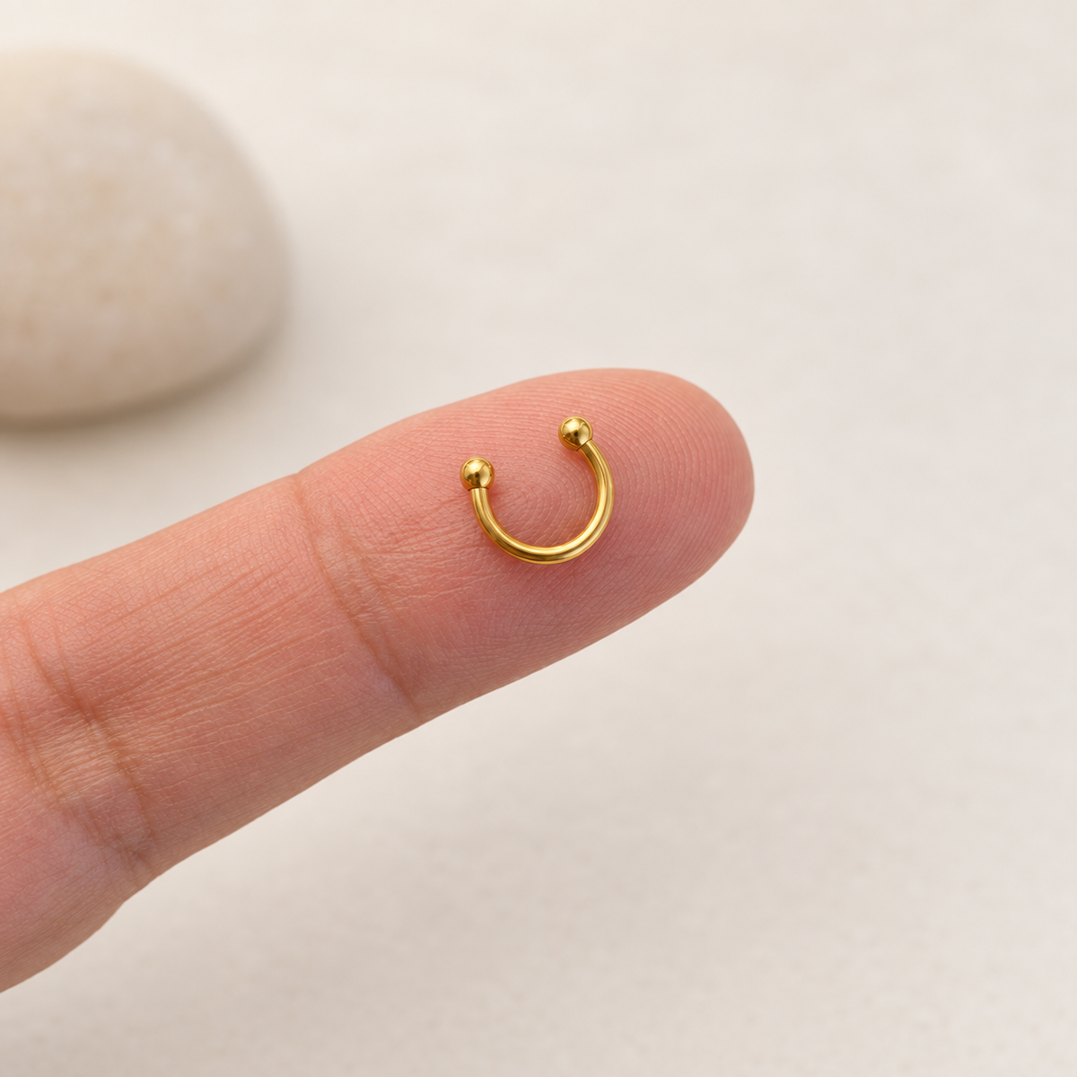 Gold mini horseshoe circular barbell on fingertip