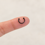Black mini horseshoe circular barbell on fingertip