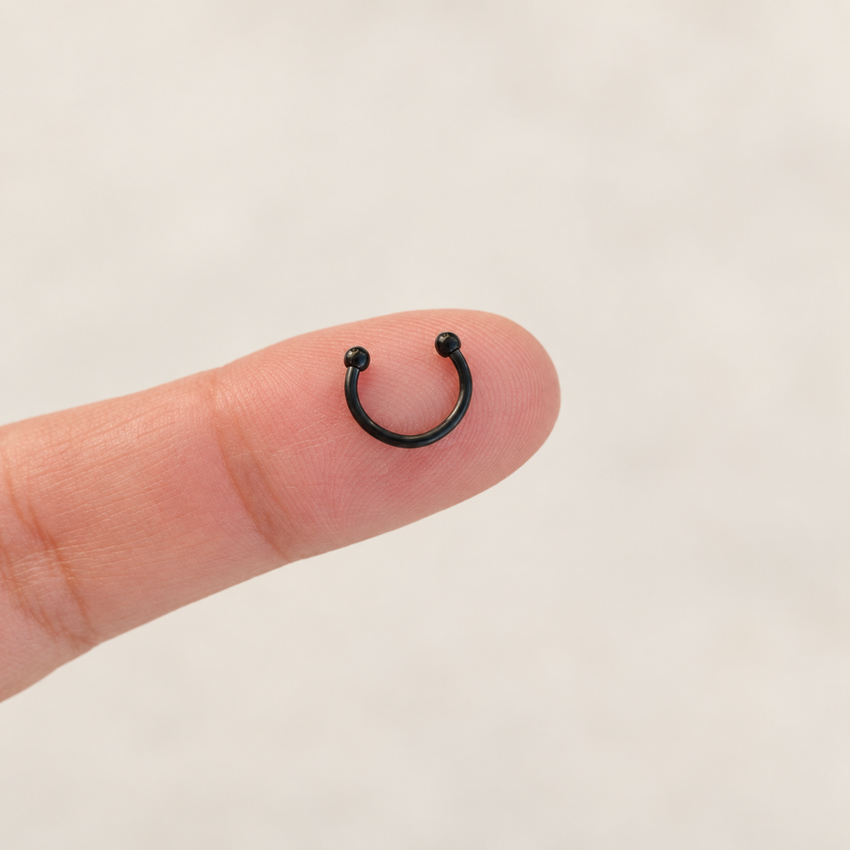 Black mini horseshoe circular barbell on fingertip