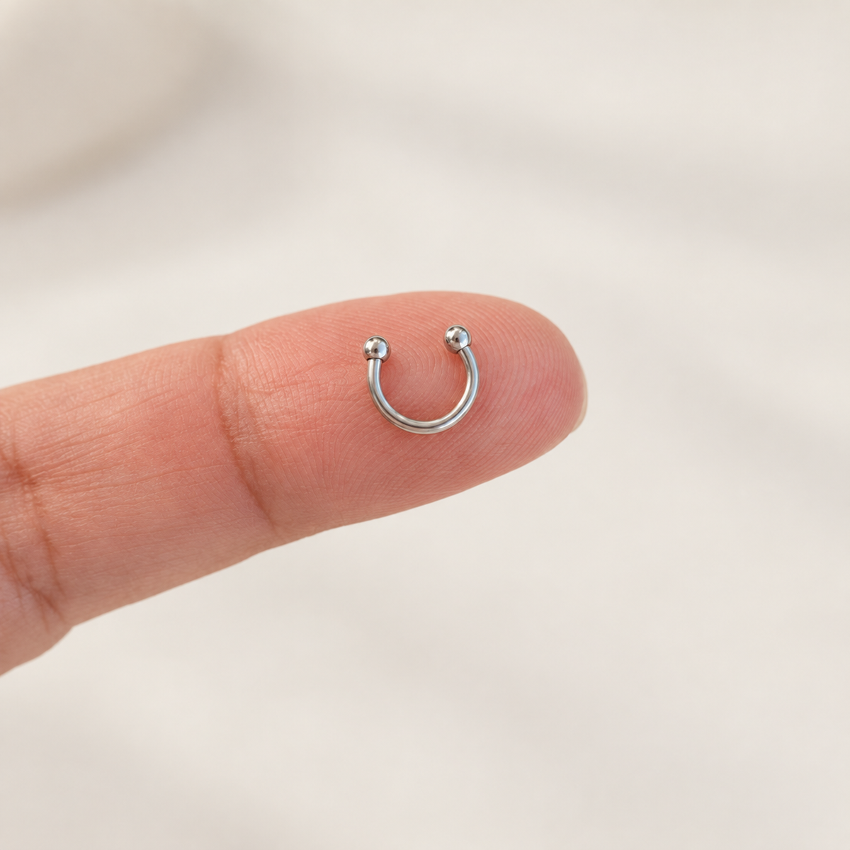 Silver mini horseshoe circular barbell on fingertip
