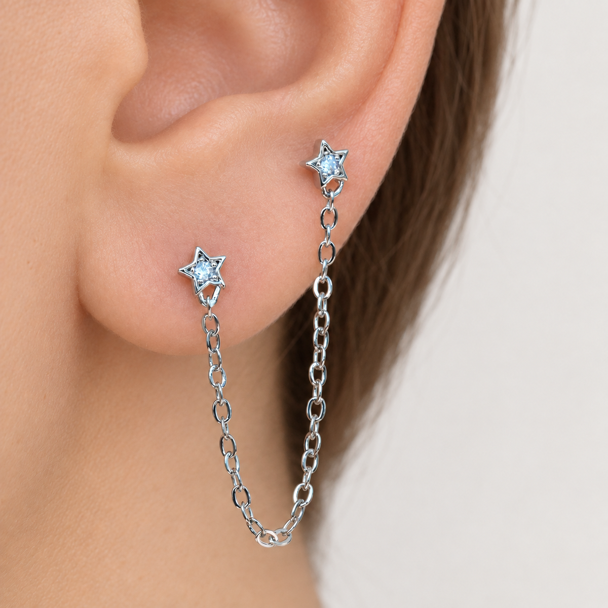 Silver star ear chain earring worn across two ear piercings