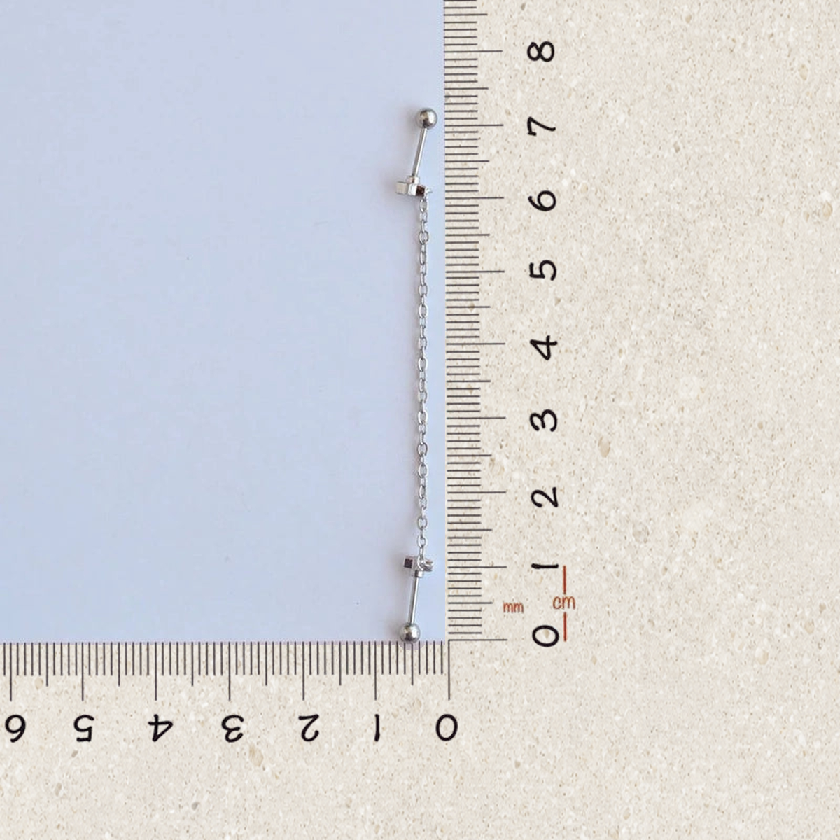 Silver star ear chain earring beside a ruler, size guide
