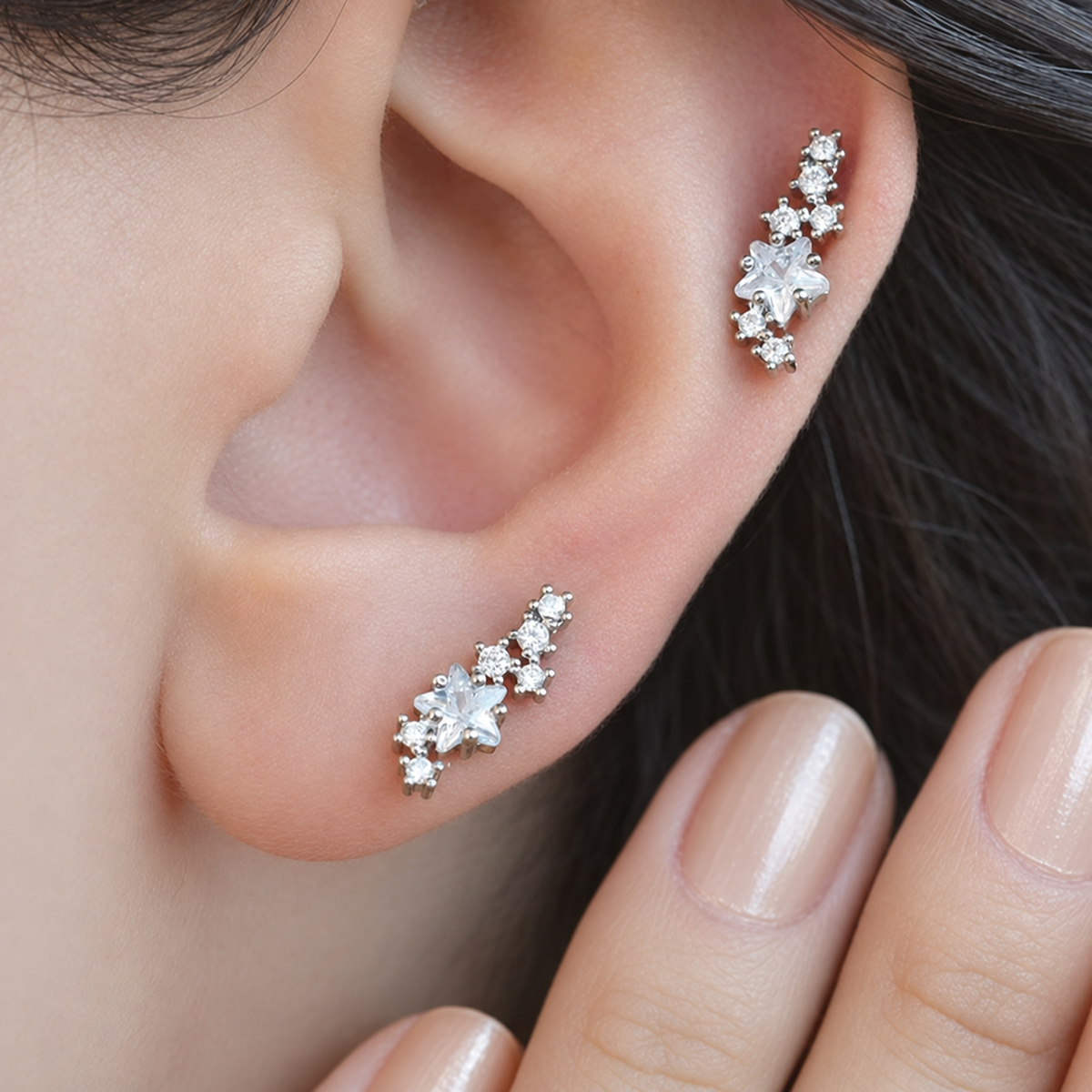 Two silver-tone star-cluster studs with clear stones worn on the earlobe and upper cartilage.