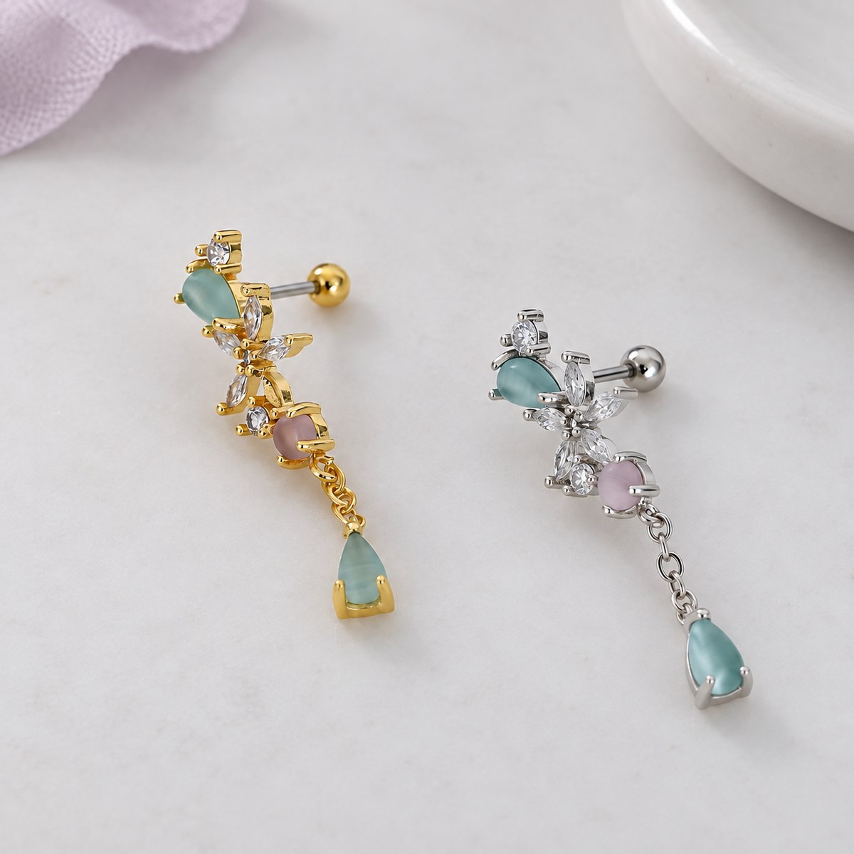 Gold-tone and silver-tone floral piercing studs with aqua and pink stones, dangling teardrops and ball backs, displayed side by side.