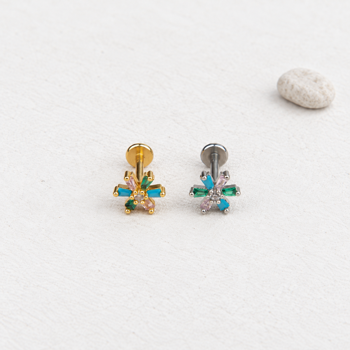 Gold-tone and silver-tone multicoloured flower piercing studs side by side, with straight posts and flat disc backs visible.