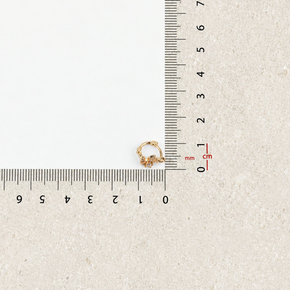 Gold leaf hoop earring against measurement ruler