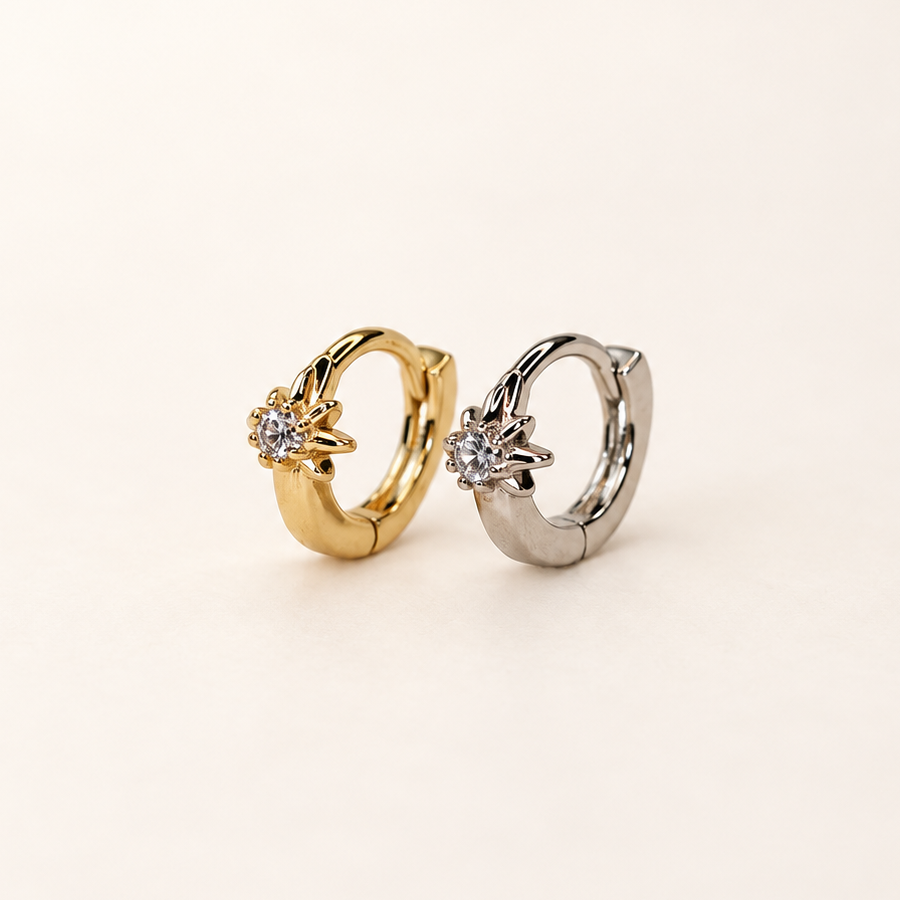 Gold-coloured and silver-coloured hoop earrings standing side by side, each with a clear stone in a star-shaped setting.