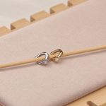 Gold-coloured and silver-coloured star hoop earrings resting on a wooden stick over a pale display pad.