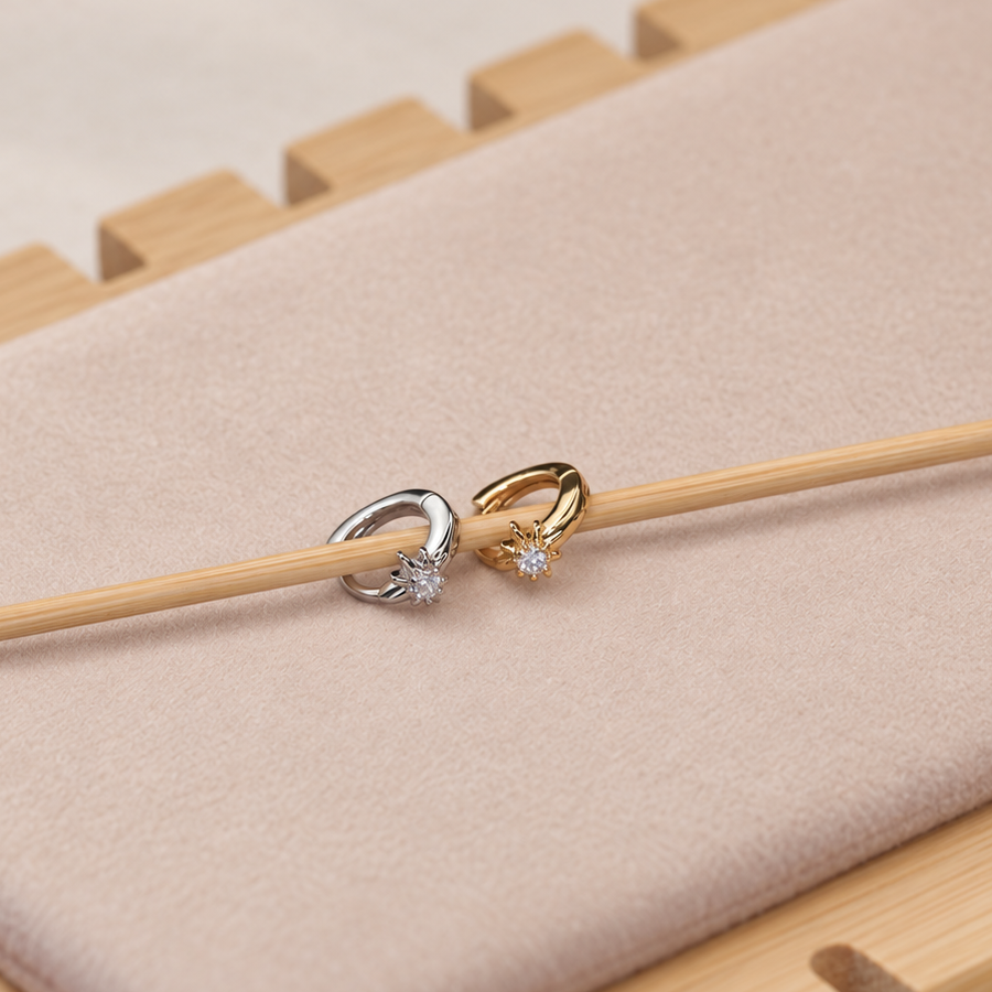 Gold-coloured and silver-coloured star hoop earrings resting on a wooden stick over a pale display pad.