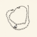 Two silver-coloured elongated-link bracelets with lobster clasps, extension chains and half-heart charms on a pale surface.