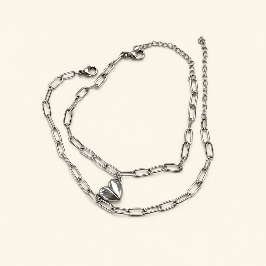 Two silver-coloured elongated-link bracelets with lobster clasps, extension chains and half-heart charms on a pale surface.