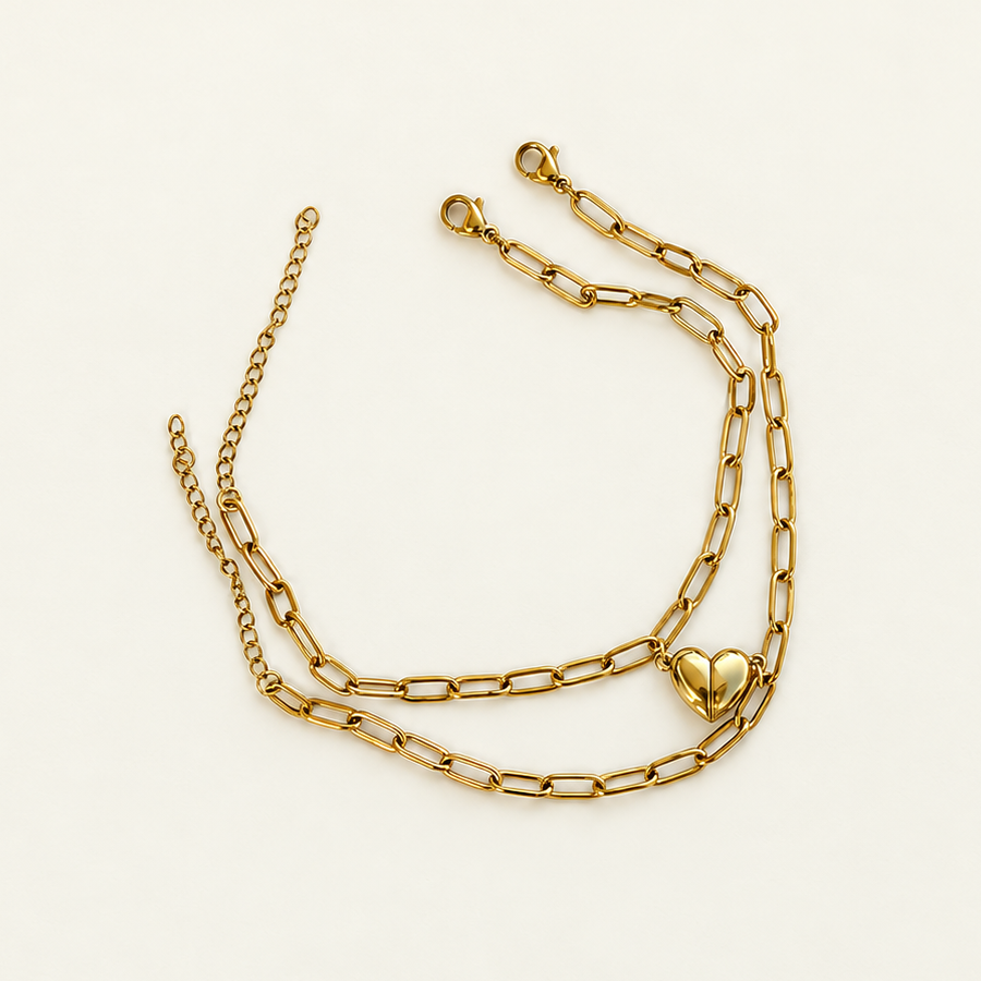 Two gold-coloured elongated-link bracelets with extension chains and joined half-heart charms laid on a pale surface.