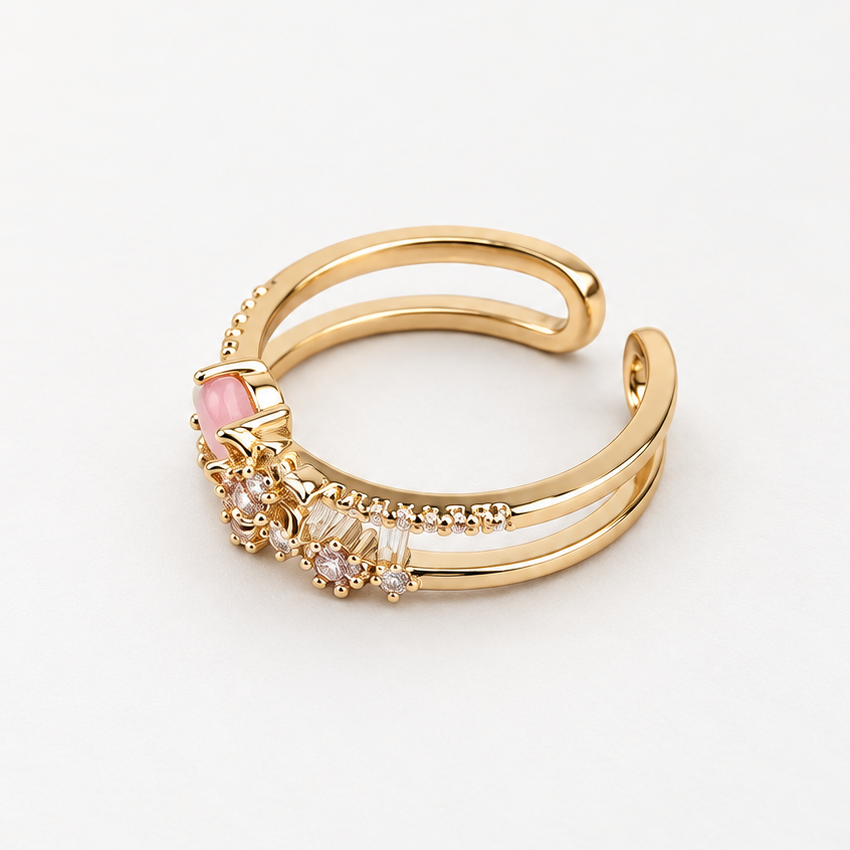 Gold-tone double-band ring on a white surface, showing its open back, pink round stone and flower details.