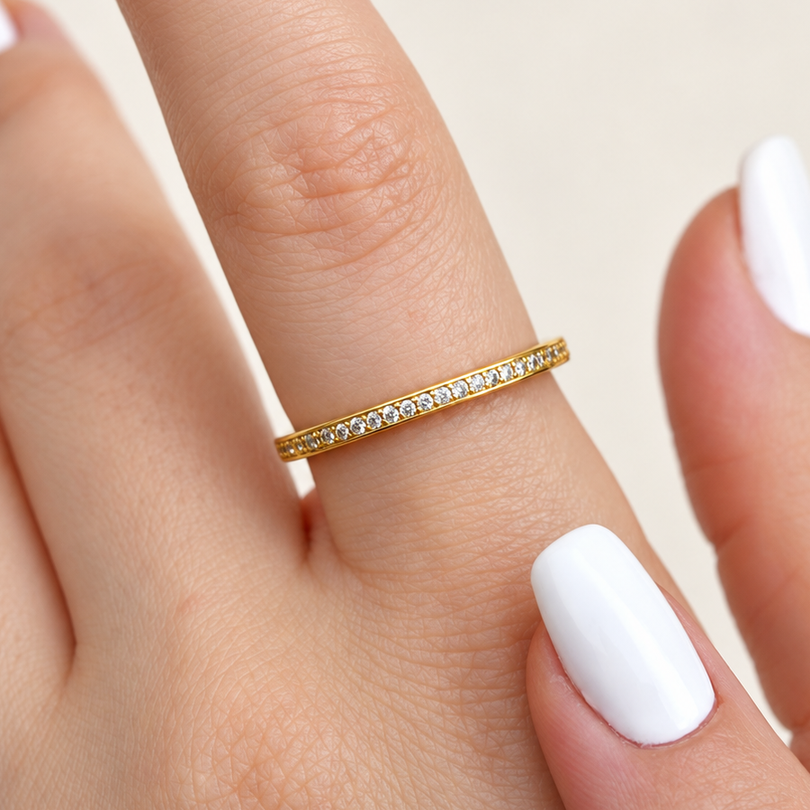 Slim gold-coloured ring with a row of round clear stones worn on a finger, beside a white-painted thumbnail.