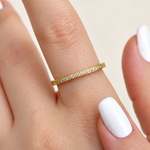 Slim gold-coloured ring with a row of round clear stones worn on a finger, beside a white-painted thumbnail.