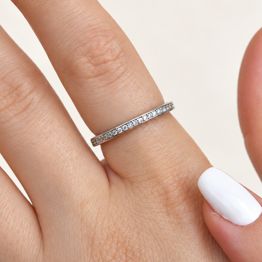 Slim silver-coloured ring with a row of round clear stones worn on a finger, beside a white-painted thumbnail.