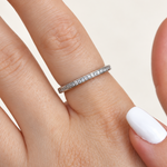 Slim silver-coloured ring with a row of round clear stones worn on a finger, beside a white-painted thumbnail.