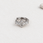 Silver-tone hoop earring with clear stones and an eye-shaped centre resting closed on a pale surface.