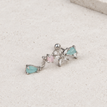 Silver-tone floral piercing stud with clear stones, aqua teardrops and a pink round stone lying on a pale surface.