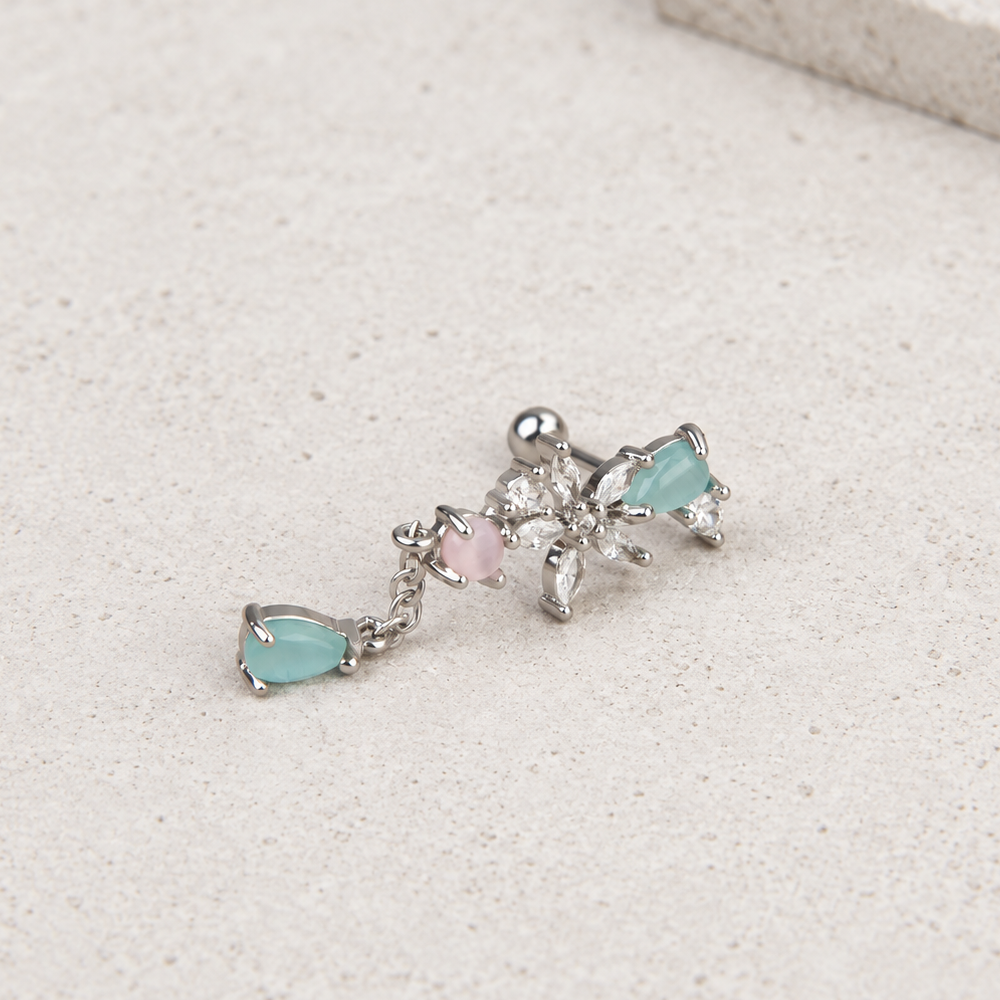 Silver-tone floral piercing stud with clear stones, aqua teardrops and a pink round stone lying on a pale surface.