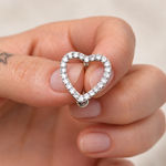 Silver-tone open-heart belly bar outlined with clear stones, held between fingers.