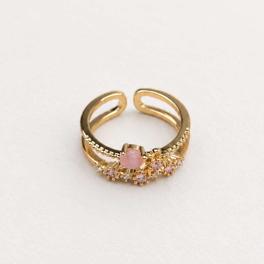 Gold-tone open double-band ring with a flower and pink and purple stones on a white surface.