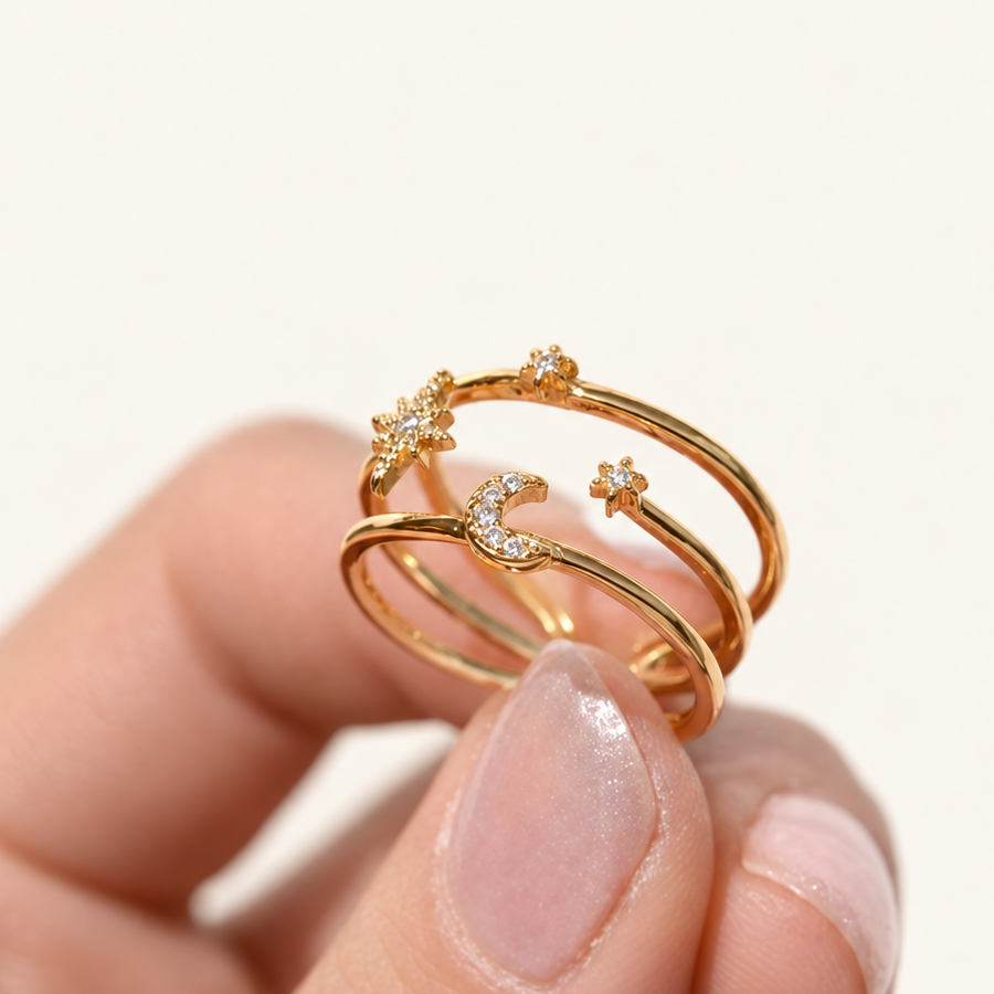 Gold-tone three-band ring with clear-stone stars and a crescent moon held between fingers.