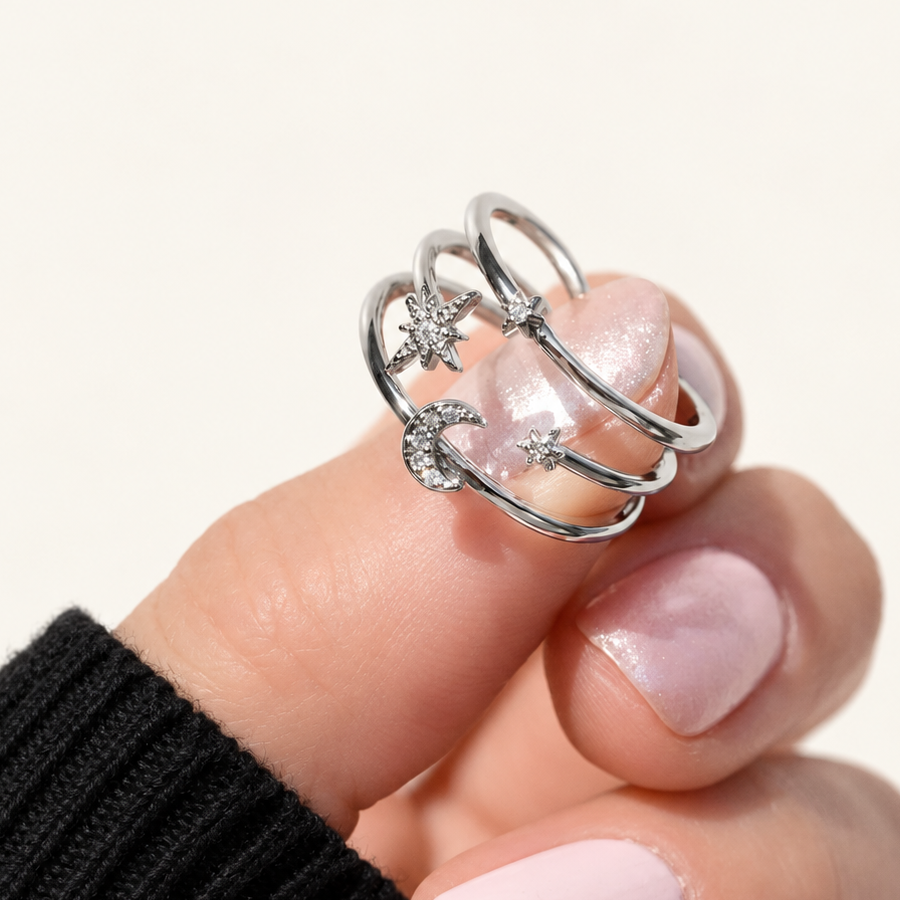 Silver-tone three-band ring with clear-stone stars and a crescent moon held against a fingertip.