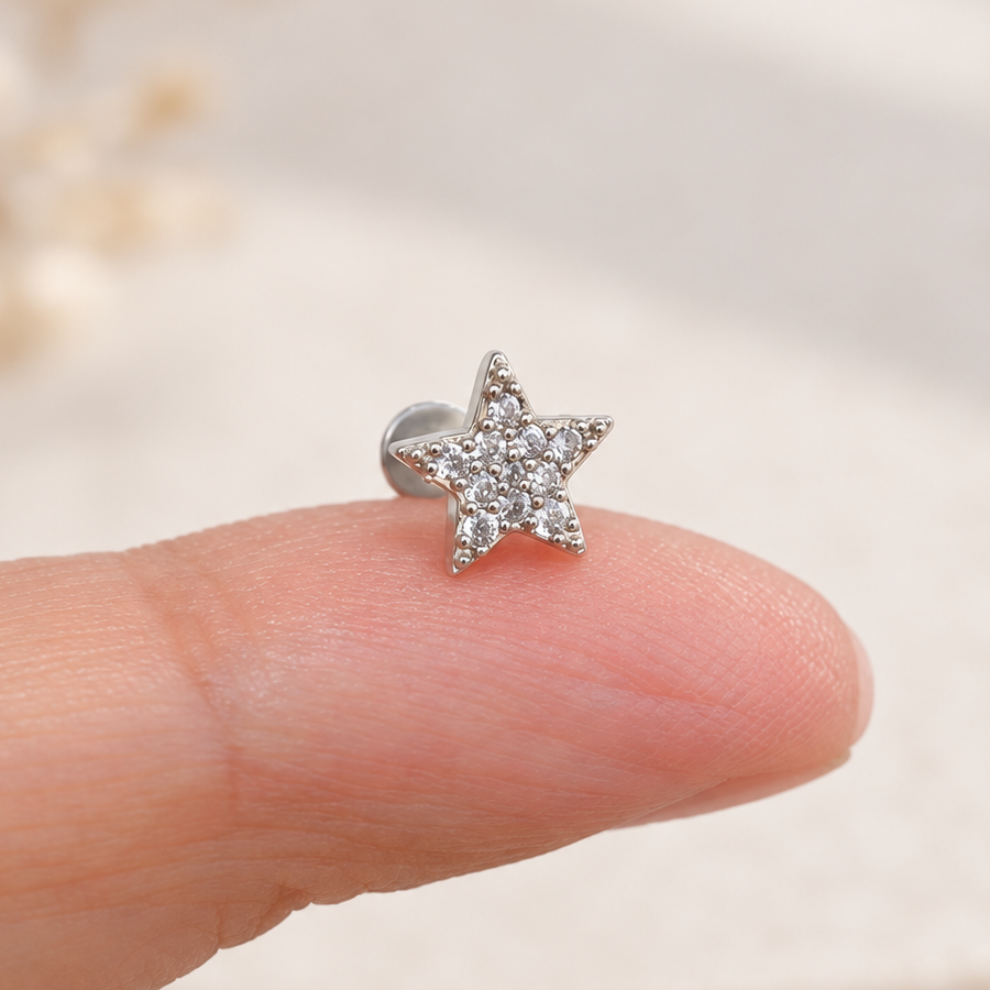 Silver-tone five-point star piercing stud covered with clear stones resting on a fingertip.