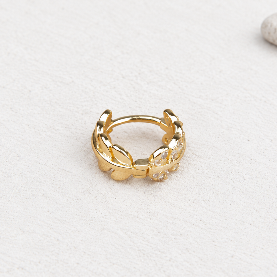 Gold-tone leaf hoop earring with clear-stone details on a pale surface.