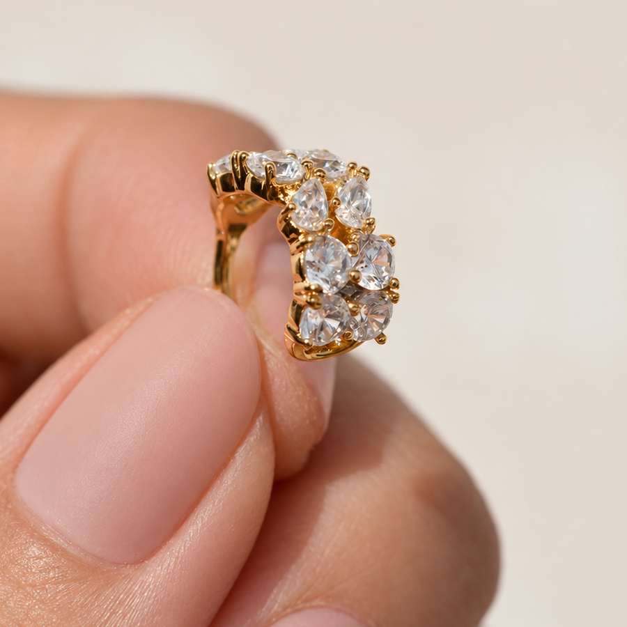Gold-tone ear cuff with rows of clear round and teardrop-shaped stones held between fingers.