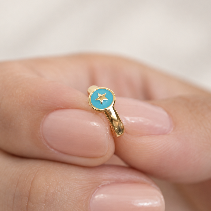 Gold-tone hoop with a turquoise-blue round face and a gold-tone star held between fingers.